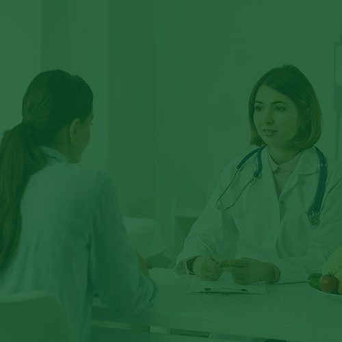 Consulta médica entre duas mulheres, com uma médica usando jaleco e estetoscópio, em ambiente profissional com mesa branca e itens de saúde.