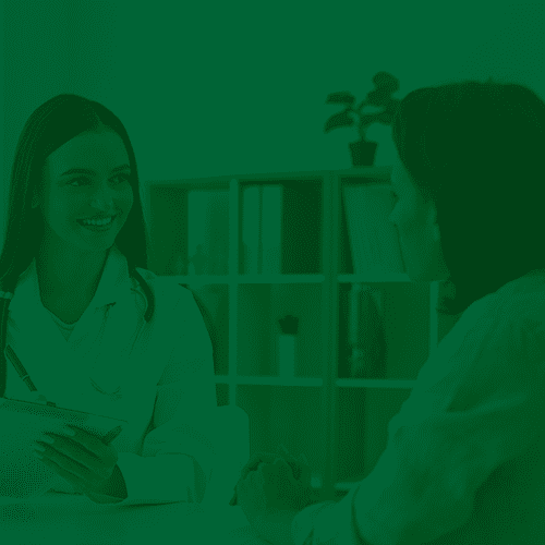 Médica sorridente conversa com paciente em consultório, segurando uma prancheta e demonstrando atendimento humanizado e acolhedor.
