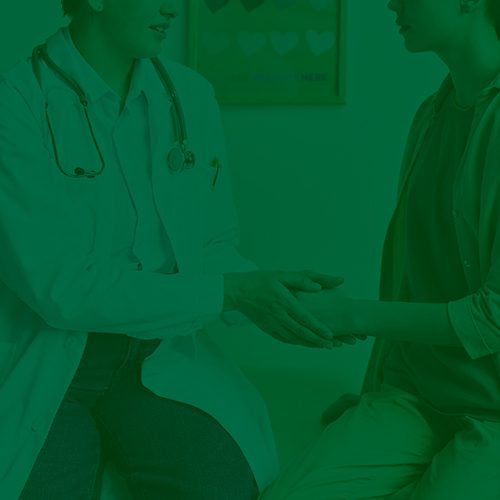 Médica com estetoscópio segura a mão de paciente durante atendimento, transmitindo acolhimento e cuidado em consultório.