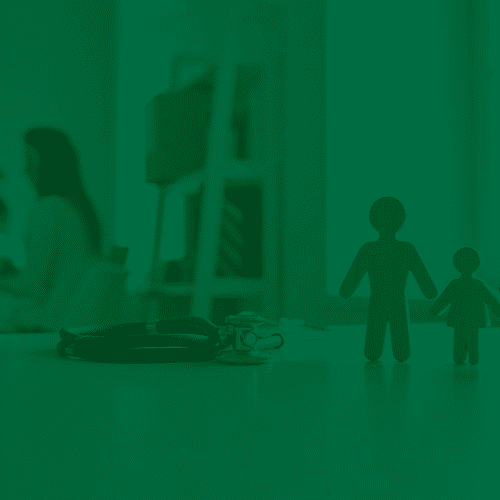 Miniaturas de família sobre mesa com estetoscópio ao lado, em ambiente de consultório médico ao fundo.