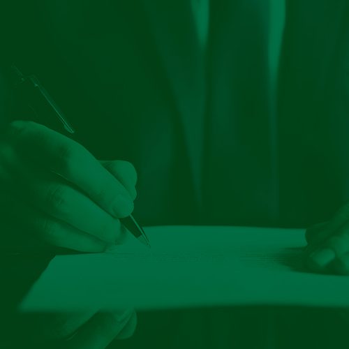 Pessoa segurando caneta enquanto assina documento sobre a mesa, em momento de formalização ou contratação.