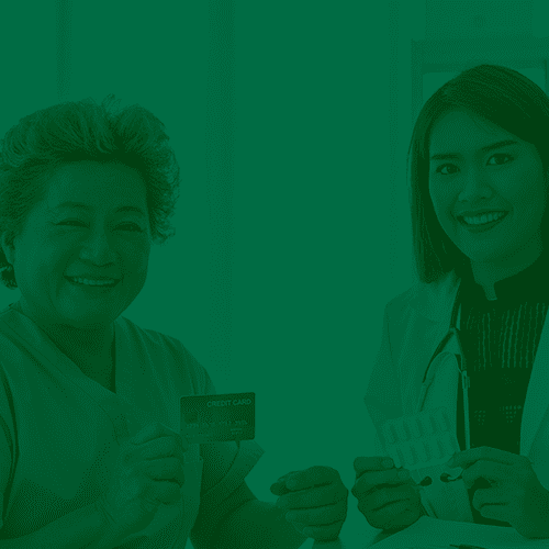 Duas mulheres sorrindo, uma profissional de saúde e uma paciente, segurando cartão e cartela de medicamentos em ambiente clínico.